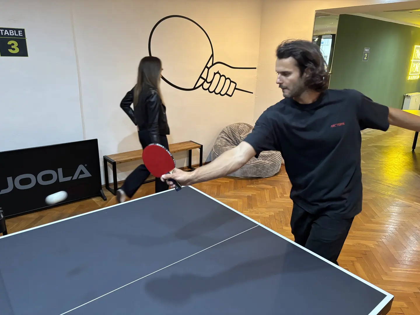 Spieler mit rotem Schläger beim Vorhandschlag an Tisch 3 im Ping Pong Garden Salzburg